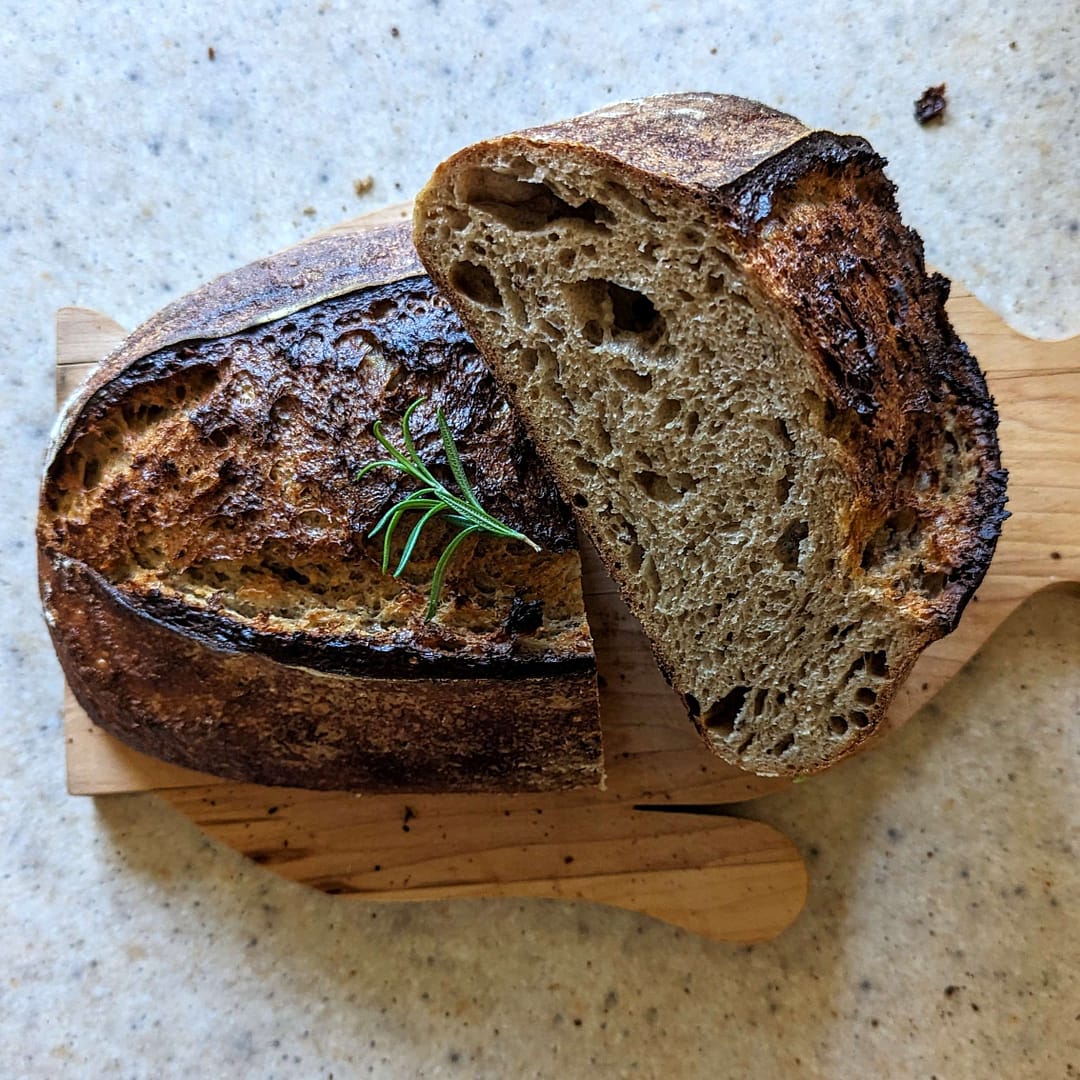 A loaf of bread with rosemary sprigs on a cutting board, perfect for Recipes and Courses.